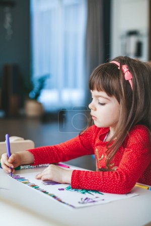 Entzückendes kleines Mädchen im Alter von 4-5 Jahren, das mit Filzstiften eine fröhliche Weihnachtsszene zeichnet. Konzept Weihnachtswerkstatt.