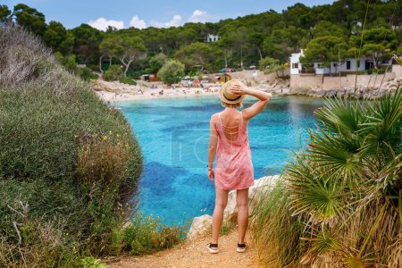 Eine Frau steht auf einer Klippe und genießt an einem Sommertag den Blick auf den Strand von Cala Gat auf Mallorca
