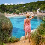 A woman standing on a cliff, enjoying the view of Cala Gat beach in Mallorca on a summer day