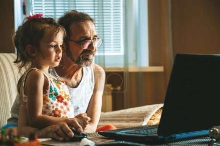 Photo for A cute little girl and her grandfather using a laptop, demonstrating a modern-day moment of connection and digital interaction. Two generations learning how to use technologies. - Royalty Free Image