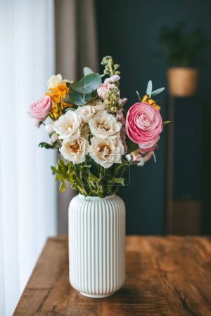 Ein lebendiger Blumenstrauß in verschiedenen Farben und Typen, arrangiert in einer weißen, gerippten Vase auf einem Holztisch
