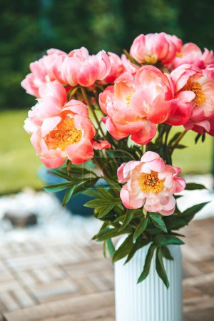 Téléchargez les photos : Pivoines roses luxuriantes remplissent un vase blanc avec crête verticale, créant un affichage vibrant - en image libre de droit