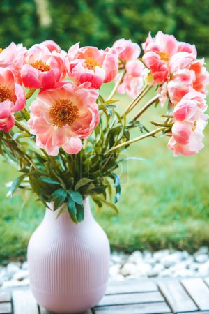 Un vase rose texturé avec des crêtes verticales présente un bouquet de pivoines roses vibrantes