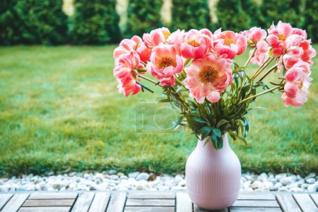 A bouquet of vibrant pink peonies with copy-space. These flowers are housed in a pink, ribbed vase, which is placed on a wooden floor
