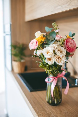 Téléchargez les photos : Un magnifique bouquet de fleurs assorties dans un vase en verre clair avec un ruban rose, sur fond de cuisine contemporaine - en image libre de droit
