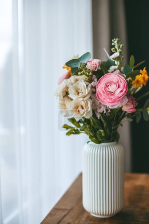 Un bouquet de fleurs vif, orne un vase blanc côtelé sur une surface en bois, situé près de la fenêtre