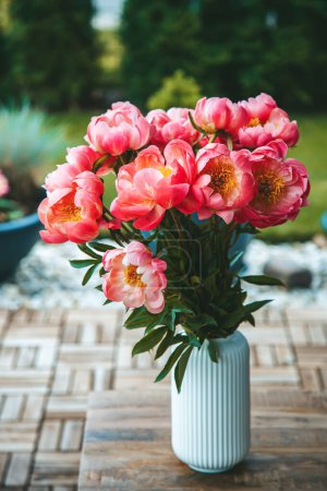 Pink peonies, vibrant and full, are arranged in a white vase textured with vertical ridges