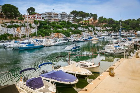 Téléchargez les photos : Au milieu de la tranquillité du port de Porto Cristo à Majorque, des bateaux amarrés ornent les eaux, encadrés par la beauté côtière des bâtiments et des paysages verts - en image libre de droit