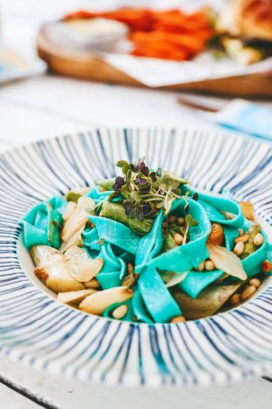 Téléchargez les photos : Gros plan Pâtes végétariennes bleu vif, complétées par des asperges, des pignons de pin et des verts, est présenté dans une assiette blanche à rayures bleues - en image libre de droit