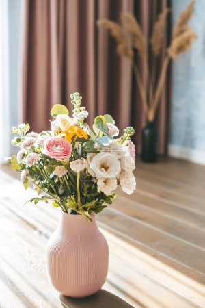 Téléchargez les photos : Un bouquet vibrant de fleurs assorties dans un vase rose texturé, placé sur un sol en bois sur fond d'élégants rideaux roses - en image libre de droit