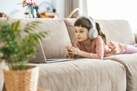 Téléchargez les photos : Une petite fille mignonne, âgée de 5-6 ans, regardant un écran d'ordinateur portable, entièrement absorbée dans son monde numérique. Concept : relaxation induite par la technologie, éducation en ligne, divertissement technologique - en image libre de droit