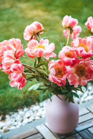 Pink peonies, vibrant and full, are arranged in a pink vase textured with vertical ridges