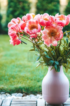 Lush pink peonies, vibrant and full, are arranged in a pink vase with vertical ridges