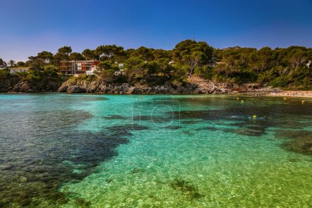 Font de Sa Cala beach in Mallorca features serene turquoise waters surrounded by rocky outcrops and lush greenery