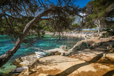 Serene view of Font de Sa Cala beach, Mallorca, with paddleboards resting on the rugged shoreline, surrounded by pristine turquoise waters and lush greenery