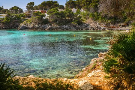Turquoise waters at Font de Sa Cala beach in Mallorca are surrounded by rugged rocks and lush green scenery