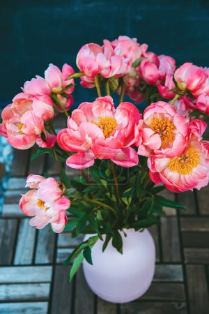 A bouquet of pink peonies, showcasing their full blossoms. The bouquet is standing in a ribbed pink vase
