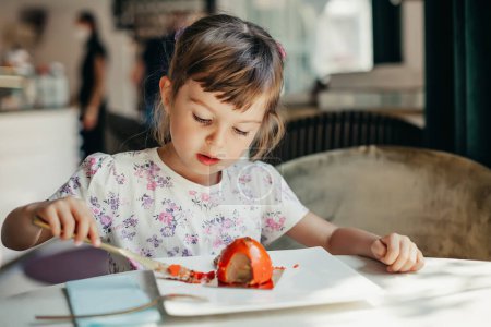 Ein süßes kleines Mädchen im Alter von 4-5 Jahren genießt ein Stück Kuchen in einem Restaurant