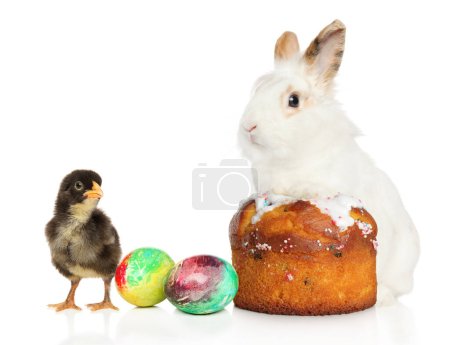Foto de Un conejo sentado en un pastel de Pascua rodeado de coloridos huevos de Pascua, junto a una pequeña gallina, sobre un fondo blanco - Imagen libre de derechos