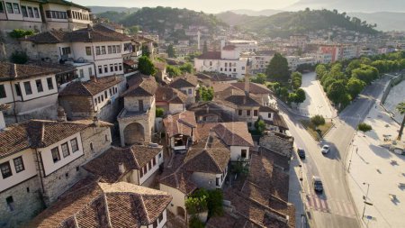 Flying over tiled roofs of houses, mosques and minarets in Berat, Albania. Magnificent Ottoman buildings in the most beautiful city of Albania - Berat. Aerial view, 4K