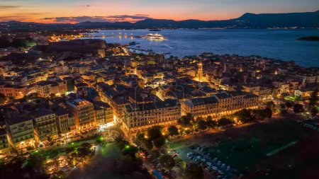 Old town with illumination against background of red sunset sky in Kerkyra, Corfu island. Evening aerial sunset view of Kerkyra, capital of Corfu island, Greece. 4K HDR shot 2