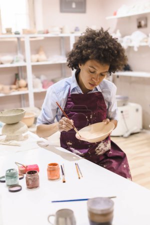Photo for Portrait of afro american woman, pottery artist, workshop, painting clay bowl. Creative craft. Ceramic studio. - Royalty Free Image