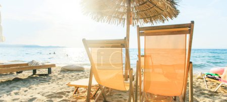 Foto de Vacaciones de verano y concepto de viaje. Sillas de playa vacías con sombrilla en la arena cerca del mar con luz solar en el fondo
. - Imagen libre de derechos