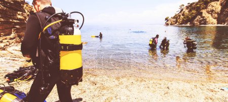 Photo for Rear view of scuba diver man with oxygen tank preparing for diving . Group of divers at the sea in background. Summer extreme activity . - Royalty Free Image