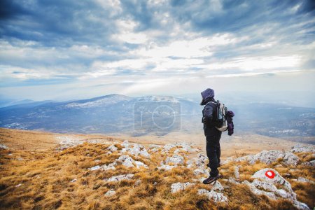 Téléchargez les photos : Randonneur avec sac à dos debout sur le sommet des montagnes, admirant le paysage de la nature hivernale, motivé à explorer. Profitez de la liberté d'un trek aventureux. Ciel dramatique . - en image libre de droit