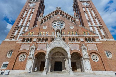 Téléchargez les photos : Une église votive en brique emblématique à Szeged, en Hongrie, avec une grande tour de l'horloge et une façade détaillée. Son importance historique se reflète dans son architecture impressionnante et son importance culturelle. - en image libre de droit