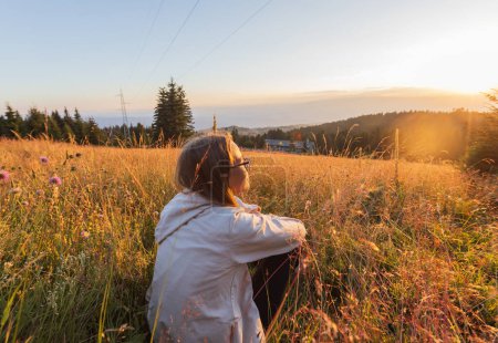Photo for Summer nature sunset, pre-teen sitting on grass, relax at meadows, enjoying evening outdoors, surrounded by beautiful landscape. - Royalty Free Image