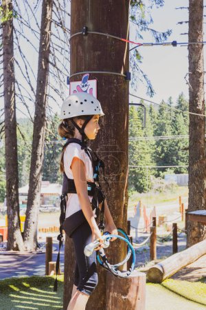Foto de Chica joven intrépida en emocionante parque de aventuras en la cima de un árbol en el corazón de un exuberante bosque durante un campamento de verano. - Imagen libre de derechos