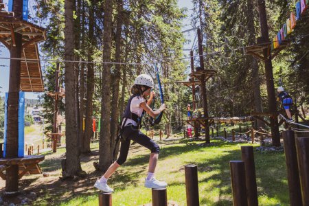 Photo for Young girl fearless at exhilarating treetop adventure park in the heart of a lush forest during a summer camp. - Royalty Free Image