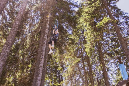 Foto de Chica joven intrépida en emocionante parque de aventuras en la cima de un árbol en el corazón de un exuberante bosque durante un campamento de verano. - Imagen libre de derechos