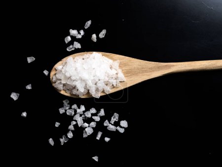 Photo for Wooden spoon with sea salt on black background - Royalty Free Image