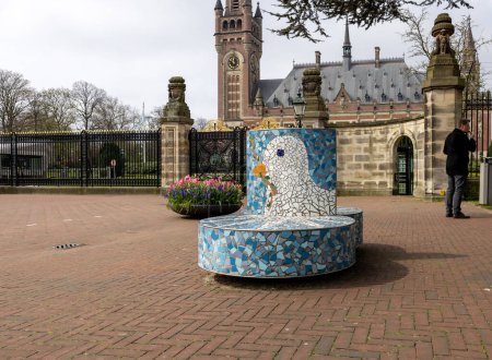Téléchargez les photos : La Haye, Pays-Bas - 17 avril 2023 : Banc avec une colombe blanche tenant une branche d'olivier symbole de paix devant le Palais de la Paix de La Haye, qui abrite la Cour internationale de justice - en image libre de droit