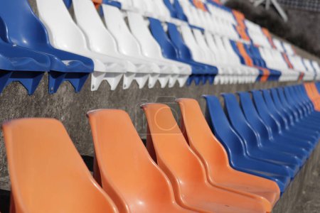 Téléchargez les photos : Une ligne lumineuse de chaises en plastique orange bordait le sol extérieur, apportant une énergie vibrante au ciel bleu - en image libre de droit