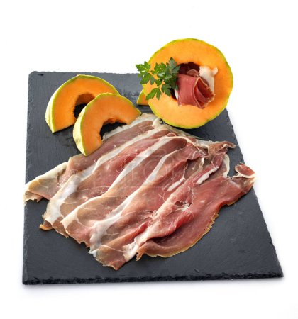 slice of cured ham serano and melon in front of white background