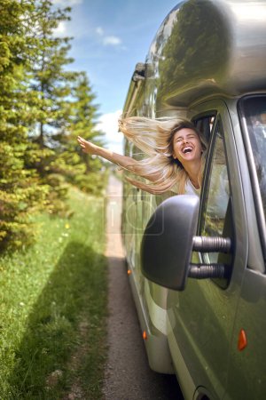 Téléchargez les photos : Belle blonde jouissant du vent conduisant dans la nature avec la tête par la fenêtre du véhicule, souriante - en image libre de droit