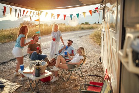 Téléchargez les photos : Groupe de personnes, hommes et femmes, socialiser, profiter en face d'un camping-car avec auvent décoré - en image libre de droit