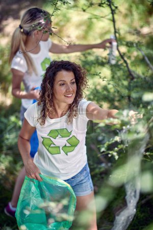 Photo for Hand picking up garbage and plastic for cleaning park or forest. Women in white shirts collecting trash in bag. Volunteers, environmentalism, lifestyle concept. - Royalty Free Image
