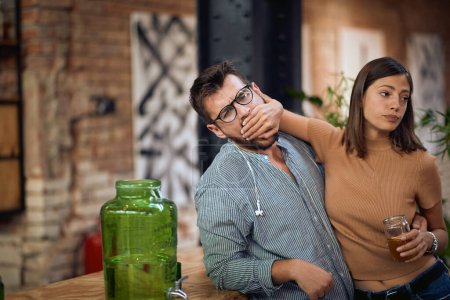 Téléchargez les photos : Jeune couple se disputant au bar. Femme tenant sa paume sur sa bouche de copains. - en image libre de droit