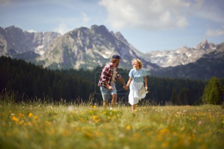 Téléchargez les photos : Couple heureux courant à travers un champ vert sur une montagne.Homme et femme souriants liberté en vacances de voyage d'été. - en image libre de droit