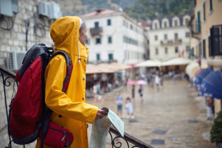 Téléchargez les photos : Une jeune touriste regarde autour de la vieille ville pendant les vacances un jour de pluie sur le bord de la mer. Vacances, tourisme, bord de mer - en image libre de droit