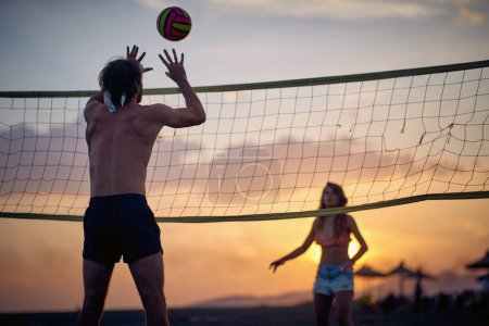 Téléchargez les photos : Un homme qui frappe une balle de volley. Groupe d'amis jouant à la plage. Sport, plaisir, convivialité, concept de style de vie. - en image libre de droit