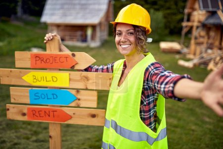 Photo for A young female builder posing for a photo at cottage construction site in the forest on a beautiful day. Workers, construction, nature - Royalty Free Image