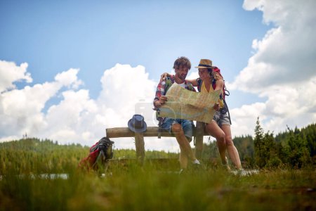 Photo for Young couple hiking in forest, looking at map and planning hike. - Royalty Free Image