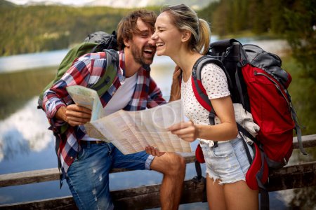 Téléchargez les photos : Homme et fille souriants au bord du lac.Couple touristes avec sacs à dos à l'extérieur. - en image libre de droit