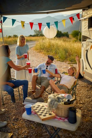 Photo for Group of friends in front of camper rv sitting and cheering with drinks. Fun, togetherness, travel, nature concept. - Royalty Free Image