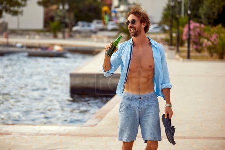 Foto de Sonriente hombre de vacaciones disfruta de un día soleado y bebe una cerveza - Imagen libre de derechos